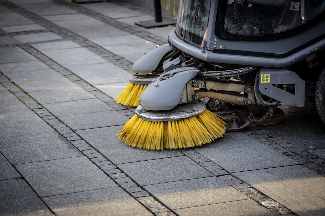 team-04 Close-up view of a road sweepers yellow brushes on a paved street.